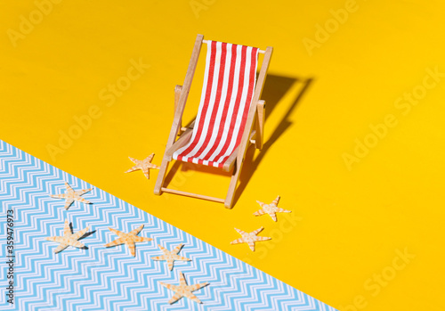 Mini beach deck chair and starfish on yellow blue background with shadow. Sunlight. Symbol of beach holidays, resort.  Relax, Summer minimal concept.