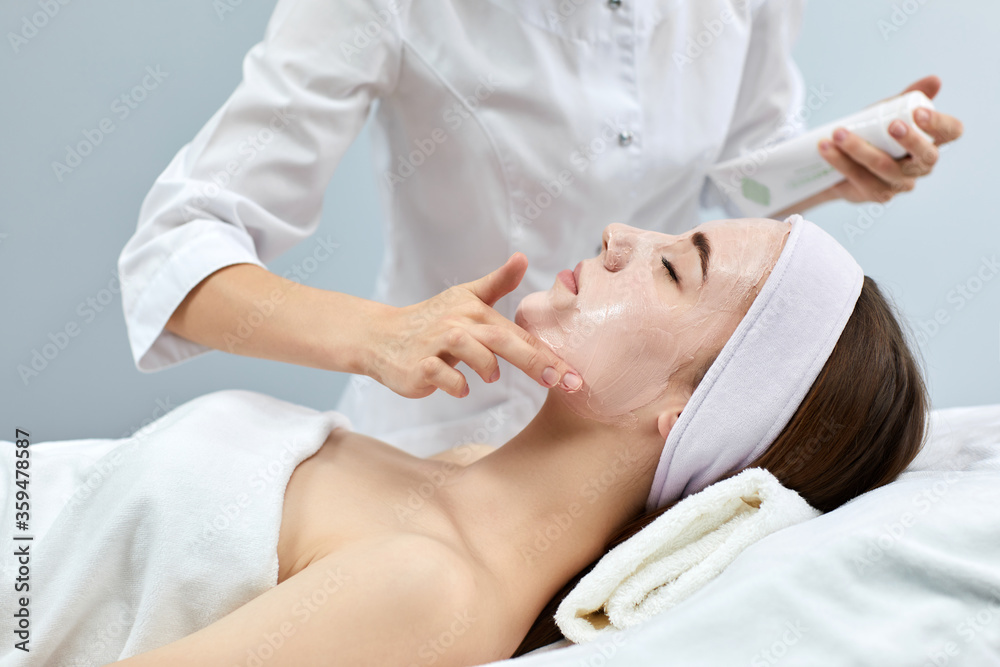 beautician applies the mask to the face of beautiful young woman in the spa salon. spa treatments beautician applies the mask to the face of beautiful young woman in the spa salon. spa treatments