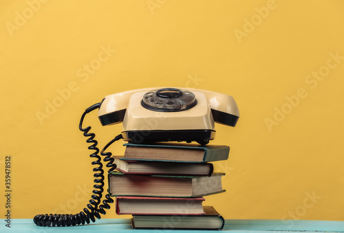 Rotary telephone on a stack of books. Yellow background photo