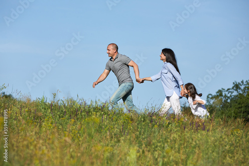 happy family father, mother and cute child girl playing and running outdoor against the blue sky