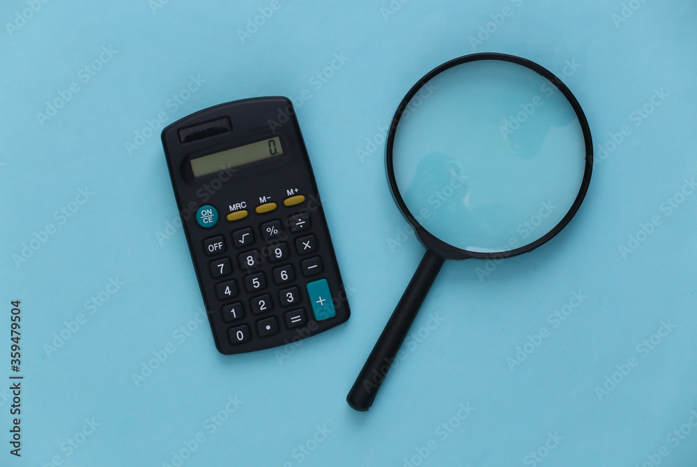 Calculator with a magnifier on a blue background. Top view Calculator with a magnifier on a blue background. Top view