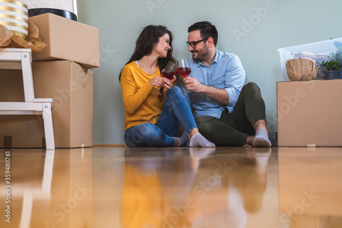 Couple celebrating moving stock photo. Husband and wife surrounded by cardboard boxes excited to move in new own house apartment