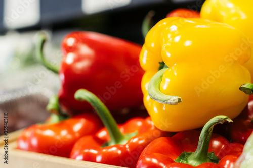 Side view of yellow bell pepper lying on red peppers on the shelf. Close-up of fresh agricultural vegetables in grocery. Vegeterian food, dieting, healthy eating.