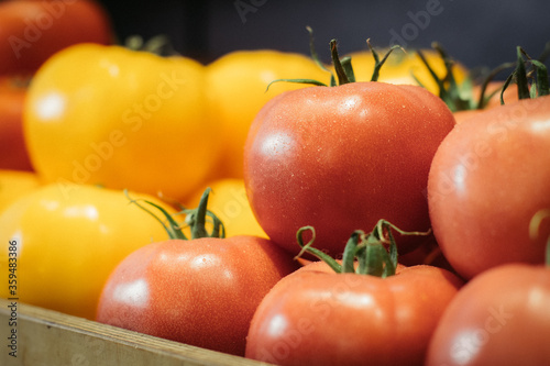 Close-up of red wet tomatoes with yellow vegetables at the background. Fresh tasty organic agricultural products lying on shelf in grocery. Healthy food, vitamin eating, assortment.