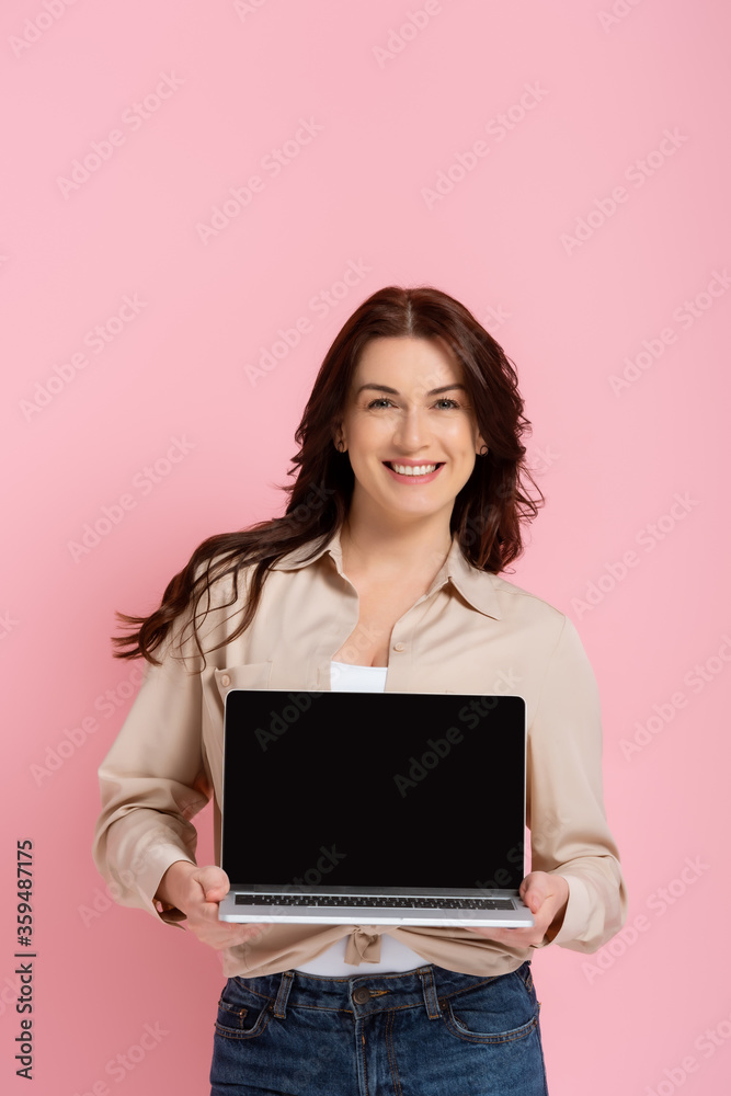 Beautiful smiling woman showing laptop with blank screen isolated on pink Beautiful smiling woman showing laptop with blank screen isolated on pink