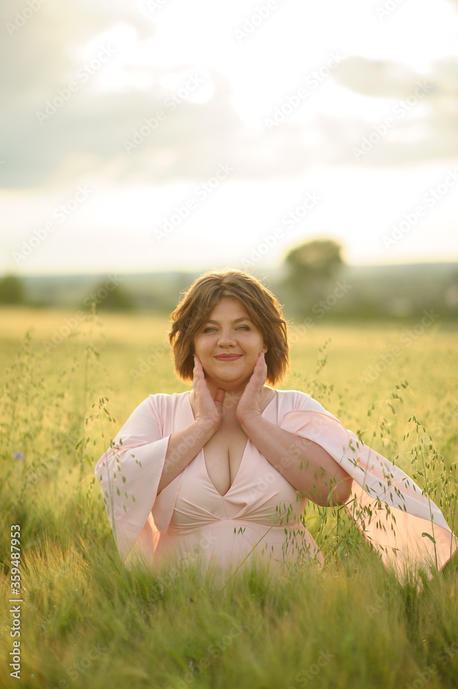 Portrait of a overweight woman in a pink dress. A woman is standing in a green wheat field. Portrait of a overweight woman in a pink dress. A woman is standing in a green wheat field.
