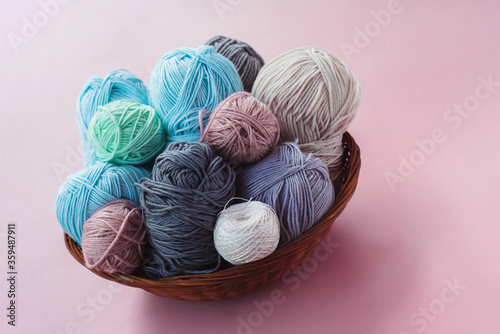  Women's hobby. Crochet and knitting. Multicolored skeins of yarn in the basket on a pink background. Studio shooting.