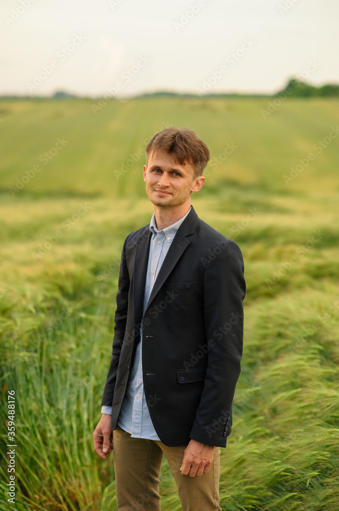 Optimistic businessman stands on a green wheat field
