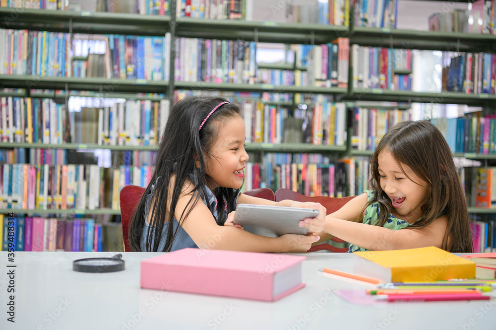 Two girls fighting for tablet in the classroom while reading books. People lifestyles and education. Young friendship and Kids relationship in school concept. Daycare and diversity theme Two girls fighting for tablet in the classroom while reading books. People lifestyles and education. Young friendship and Kids relationship in school concept. Daycare and diversity theme