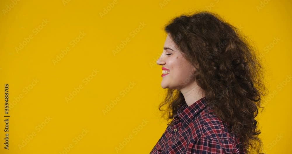 Close-up profile attractive plus-size model posing. A curly-haired brunette on a bright yellow studio background demonstrating different emotions. Girl Blowing sweet air kiss with her hand Close-up profile attractive plus-size model posing. A curly-haired brunette on a bright yellow studio background demonstrating different emotions. Girl Blowing sweet air kiss with her hand