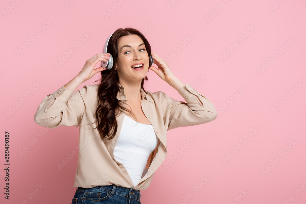 Cheerful woman in headphones looking away on pink background Cheerful woman in headphones looking away on pink background