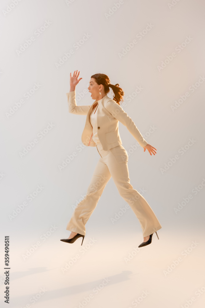 Fototapeta premium Side view of woman in formal wear jumping on grey background