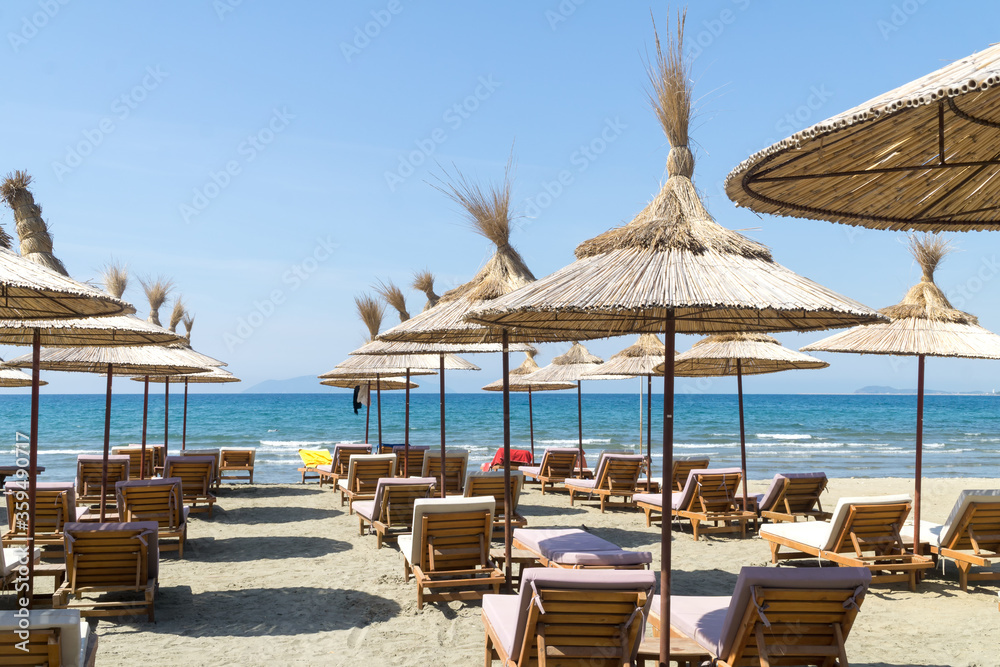 The rows of empty sunbeds with straw umbrellas on the beach. Blue sky and turquoise sea. Sunny summer day. Vlora / Vlore, Albania, Europe.