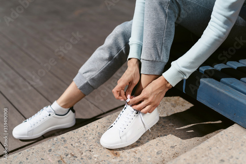 A young athletic woman preparing for training on the street, puts on sneakers and ties shoelaces. Healthy lifestyle concept. Street sport after quarantine by Covid-19 coronavirus