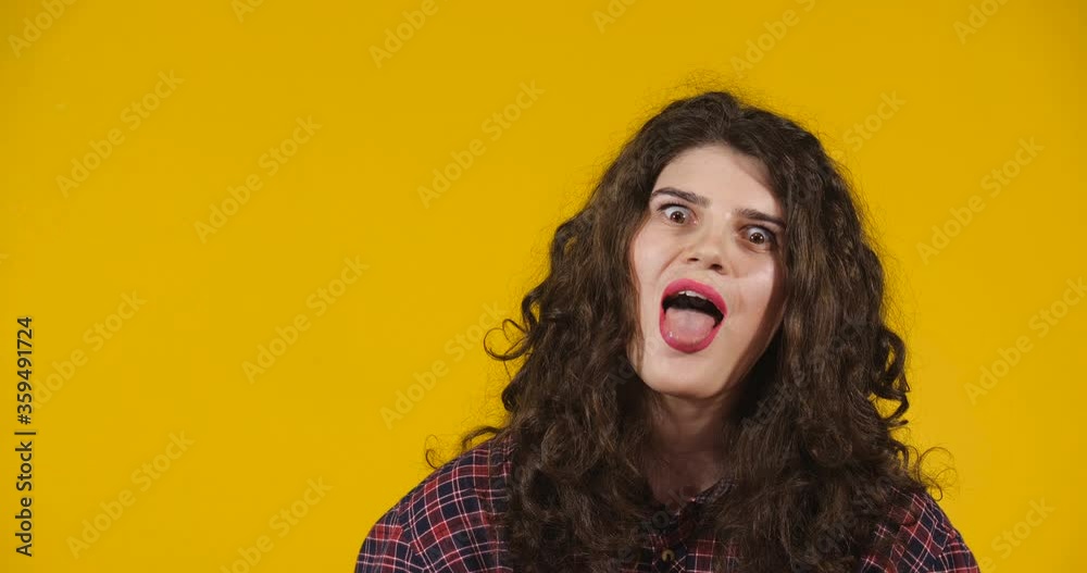 Close-up attractive plus-size model posing. A curly-haired brunette on a bright yellow studio background demonstrating different emotions. Girl flirting, making freaky faces and showing tongue Close-up attractive plus-size model posing. A curly-haired brunette on a bright yellow studio background demonstrating different emotions. Girl flirting, making freaky faces and showing tongue