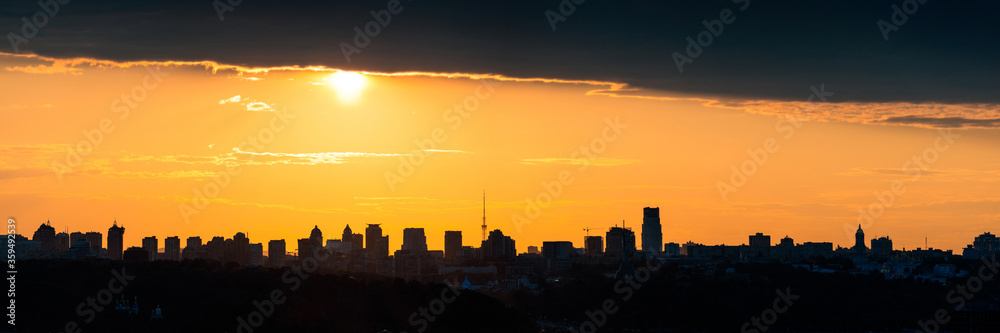 Beautiful sunset sky with clouds over city skyline background. Wide panorama of Kyiv city silhouette. Ukraine.