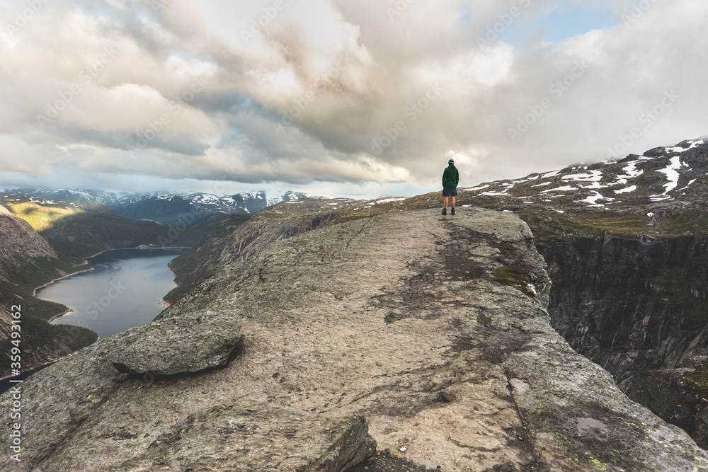 Tourist stands alone on Troll tongue rock. Famous natural landmark in Vestland county, Norway - Trolltunga. Wanderlust. Sunrise in mountains.