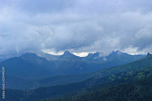 Blurry view to distant conifer forest and foggy mountains. Dark siberian taiga in haze. Low clouds over a mountain range. Landscape of hills covered in forests. Nature Park Ergaki  Russia  Siberia.