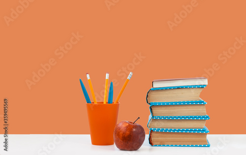 Back to school, pile of books and red apple on the white table with pink orange background. Distance home education. Quarantine concept of stay home. © Inna