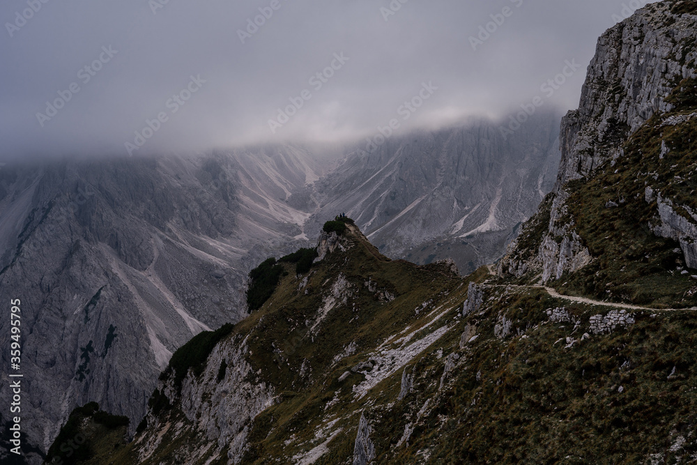 Fototapeta premium Dolomites Alps. Cadini di Misurina. Italy. Group of travellers stays on the top of the mountain in heavy fog over a cliff wrapped by white clouds