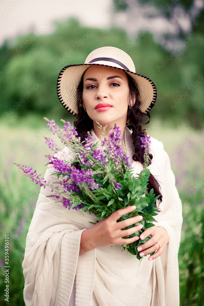 Woman in a hat holding lilac flowers on the meadow.