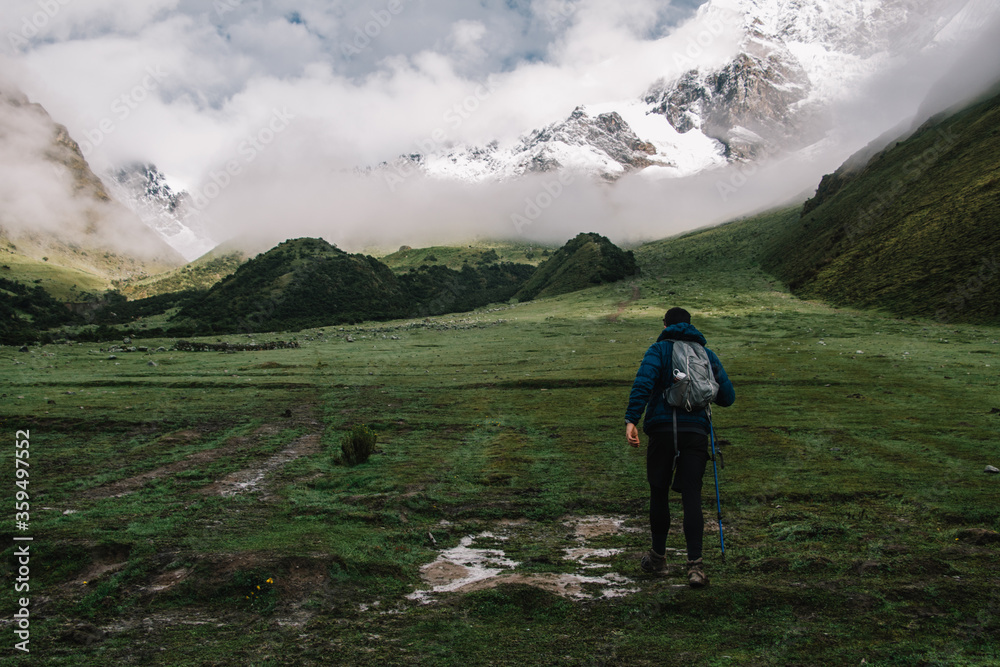 Back view of male hiker with backpack and trekking sticks travelling in Salkantay enjoying adventure in mountains.Professional traveller exploring nature environment in South America