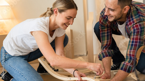 Happy Smiling Couple Collects Furniture as a Team. Girl Helps to Assemble Chair Details. Moving to New Apartment, Young Family Assemble Furniture
