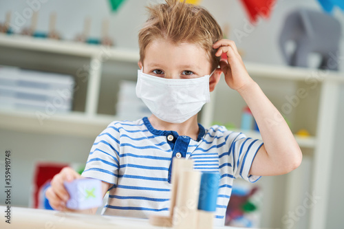 Adorable little boy in kindergarten with mask on due to coronavirus pandemic