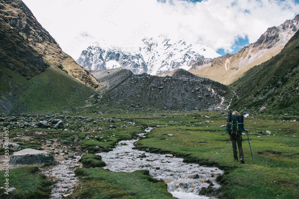 Back view of female tourist with travel backpack exploring environment of high mountains covered snow during hiking trekking in Salkantay nature.Young woman with backpack walking during trip in Peru