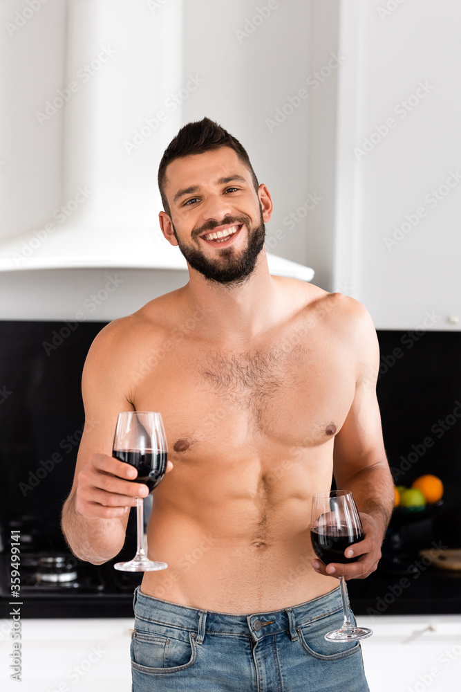 happy and shirtless man holding glasses with red wine happy and shirtless man holding glasses with red wine