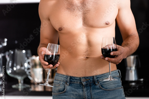cropped view of muscular man holding glasses with red wine