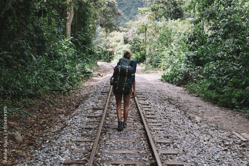 Back view of professional female hiker with tourist backpack exploring wilderness environment during hiking trekking on railway in destination of mountains and green vegetation to discover new places