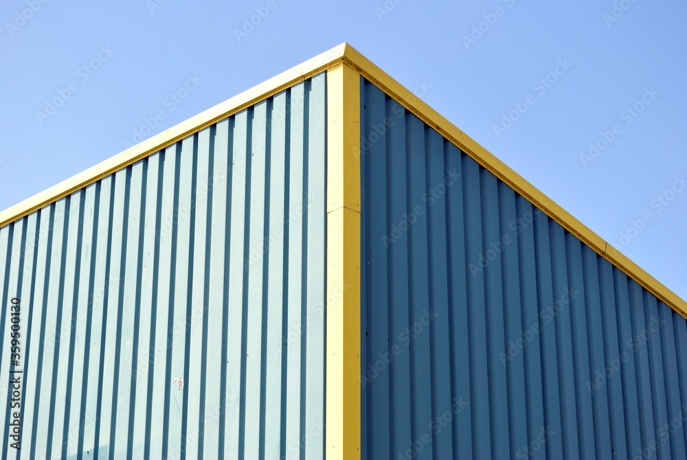 Corrugated Steel Cladding on Corner of Blue Painted Industrial Building against Blue Sky Corrugated Steel Cladding on Corner of Blue Painted Industrial Building against Blue Sky