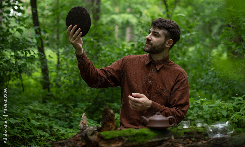 Young man holding round flat disk of shu puer tea in summer forest 