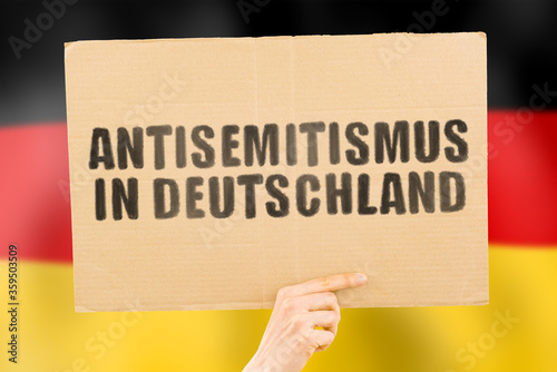 Canvas-taulu The phrase  Anti semitism in Germany  in German language on a banner in men's hand with blurred background
