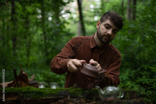 Man pouring shu puer tea in cha hai on wooden log in moss in forest © Dmytro Hai