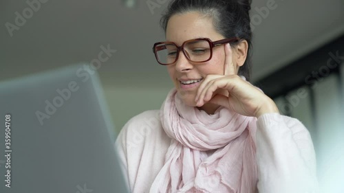 Smiling woman with dark hair drinking hot tea while connected on laptop computer
