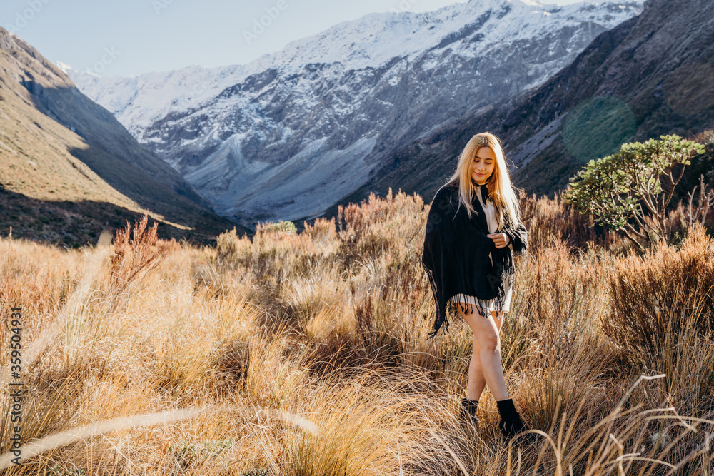 Happy asian woman relaxing on dried grass, blue sky with sunlight at sunny winter day, travel vacation, landscape snow mountains background.