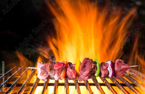 Tasty skewer on cast iron grate with fire flames. Freeze motion barbecue concept.
