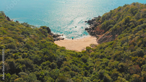 Beautiful secret beach Butterfly in Goa, India. Aerial view of pristine beach with rocky bay and waves crashing.