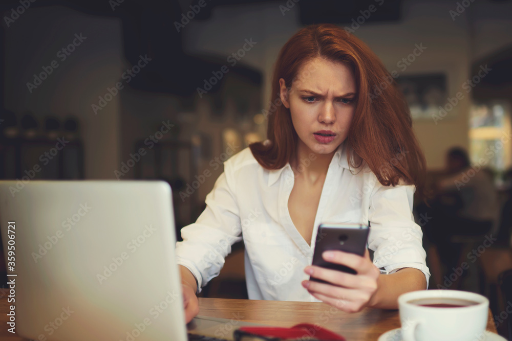 Young female skilled trader waiting for meeting with business partners sitting at table in modern coffee shop while checking email box via smartphone connected to free wireless connection to internet Young female skilled trader waiting for meeting with business partners sitting at table in modern coffee shop while checking email box via smartphone connected to free wireless connection to internet