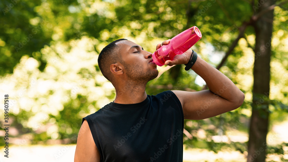 Stay hydrated. Sporty black guy drinking water from plastic bottle