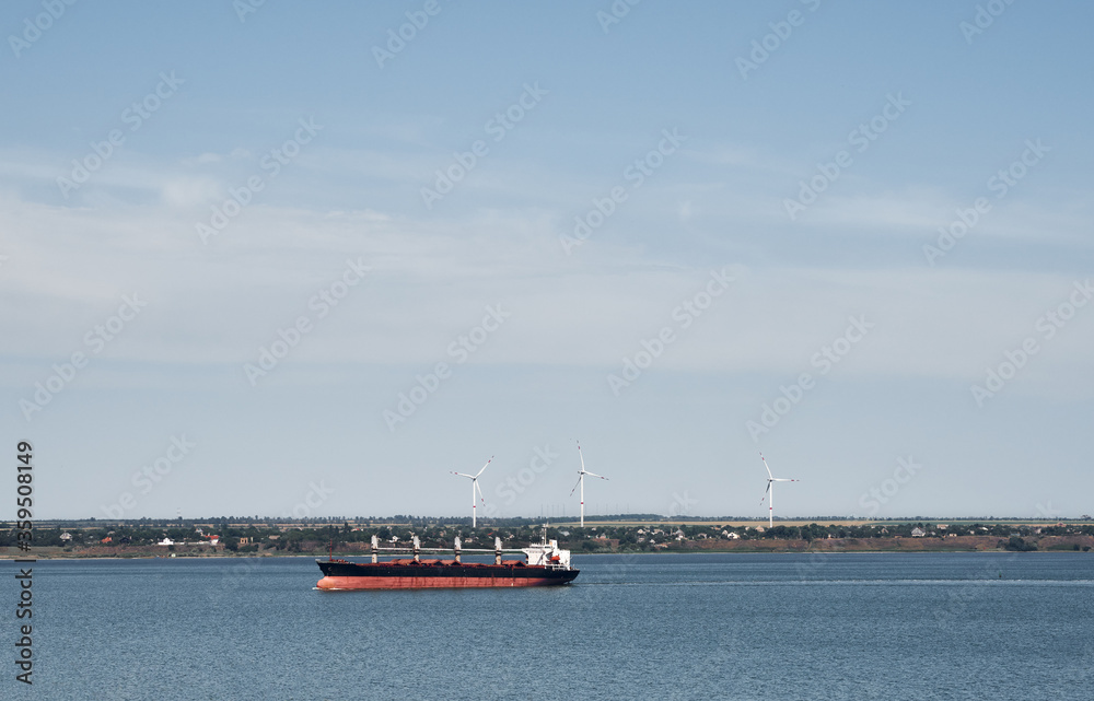 Commercial freight shipping vessel in front of wind mills. Seas cargo ship. Logistic overseas and freight services