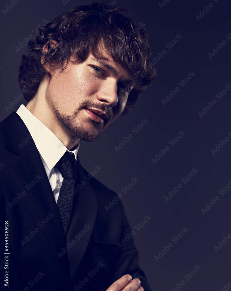 Fototapeta premium Handsome charismatic bearded man looking serious in dark shadow dramatic light with folded arms. Closeup toned color portrait