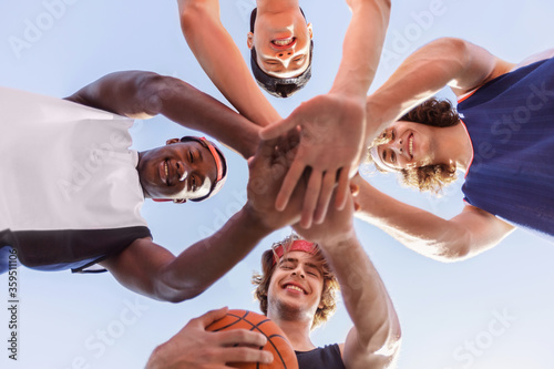Bottom view of happy multiracial basketball team putting their hands together in unity before game outside
