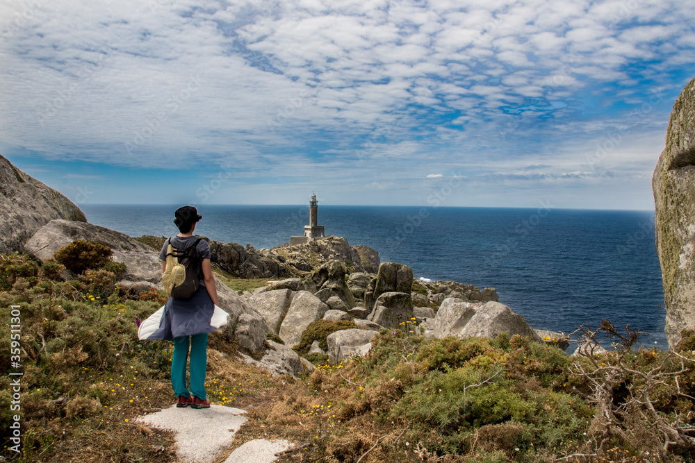 Hiker woman walks along a beautiful path and looks at the Punta Nariga lighthouse with the Atlantic sea in the background