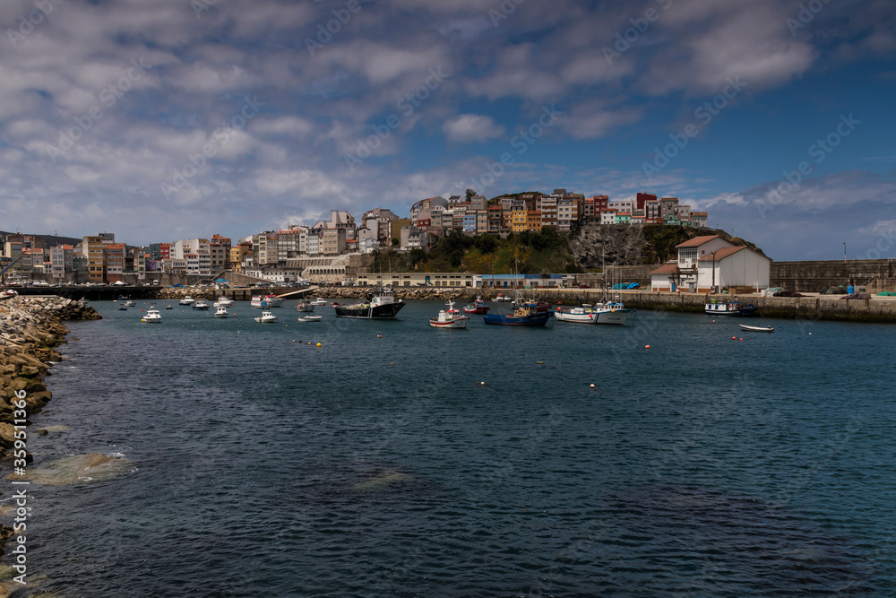 Fishing boats moored in the port of Malpica de Bergantiños under a blue sky and stratus clouds