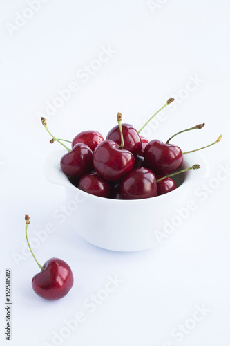 Red cherries in the white bowl on the white background. Location vertical. Copy space. © Liudmyla