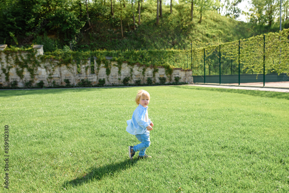 Little blond boy runs on green grass.