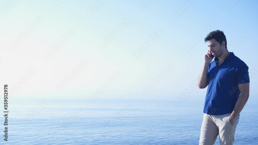 Young man talking on mobile phone while walking on beach Young man talking on mobile phone while walking on beach